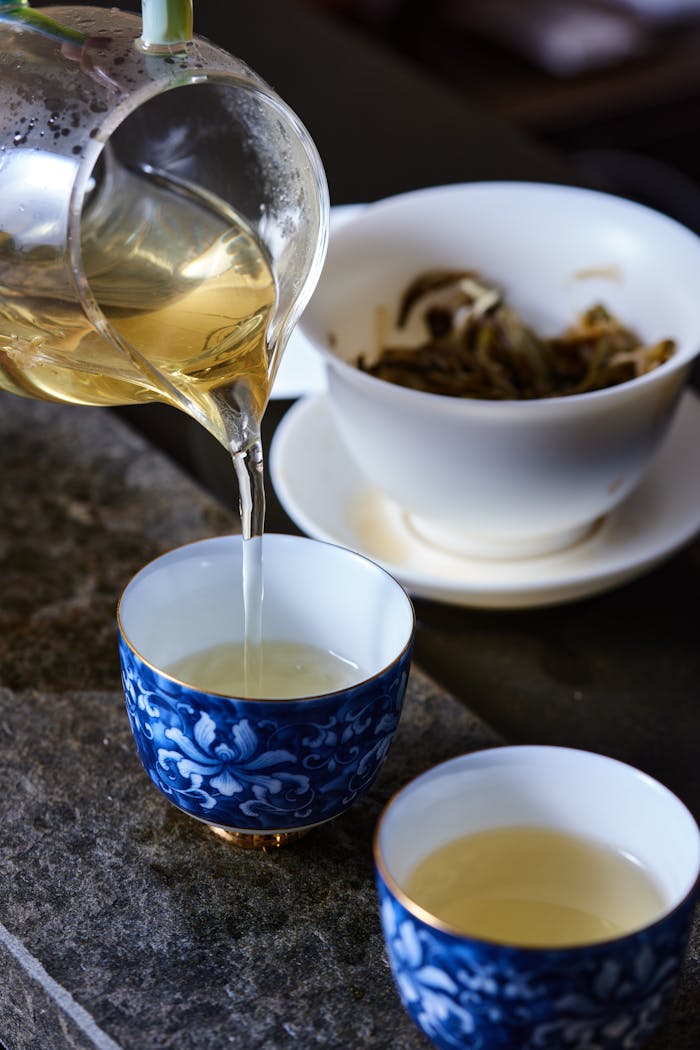 Delicately pouring tea from a glass pitcher into elegant blue porcelain cups. Still life capture.